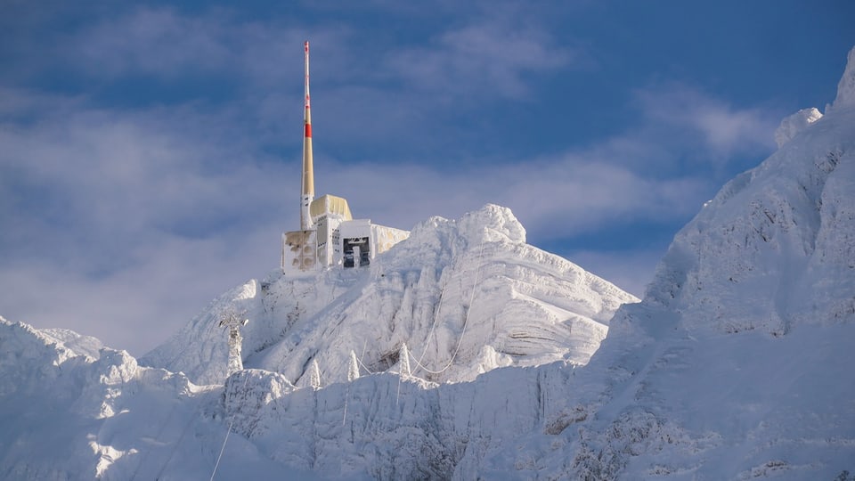 Ein schneebedeckter Berg, oben eine Gondelbahnstation. 
