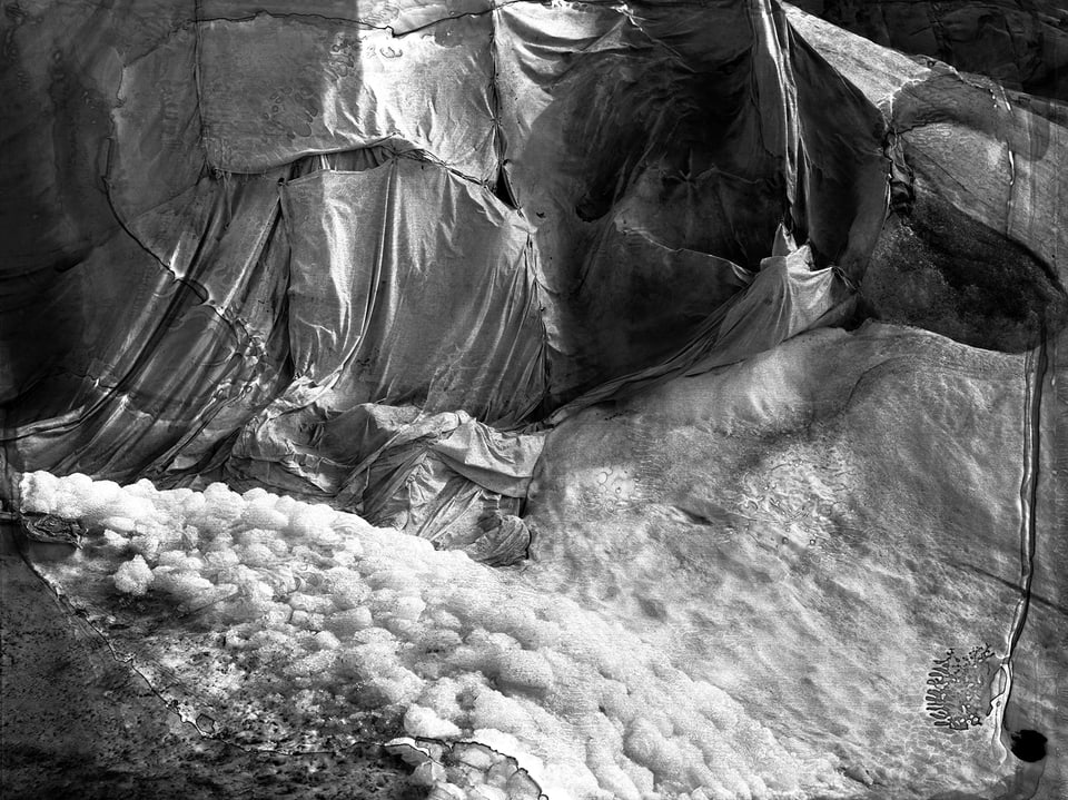 Schwarz-Weiss-Aufnahme von grossen Tüchern, auf denen Schnee liegt. 