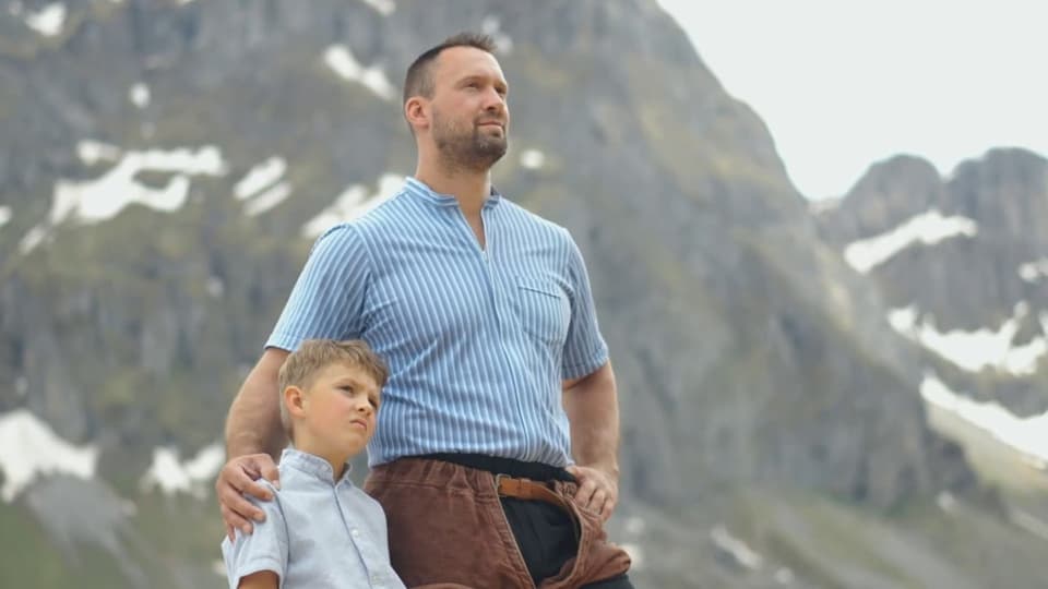 Kilian Wenger vor Bergkulisse mit kleinem Jungen im Arm.