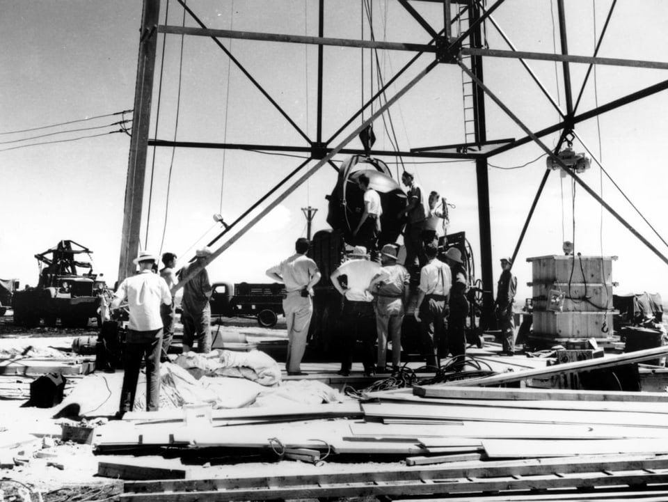 Arbeiter platzieren die erste Atombombe auf einem Turm.