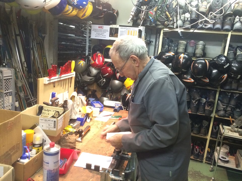 Mann steht in Raum voller Skiausrüstung vor einer Werkbank mit Werkzeugen.