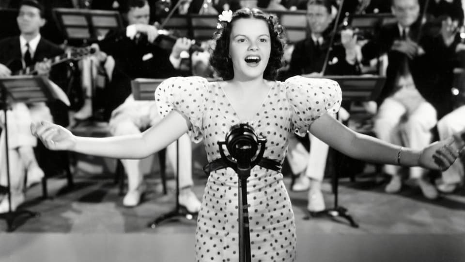 Judy Garland singt. Hinter ihr das Orchester.