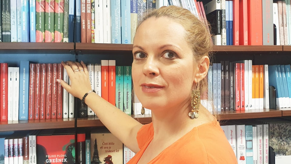 Woman with blonde hair tied back in front of a book shelf