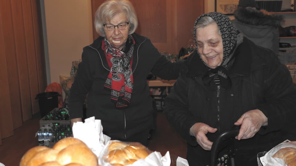 Helferin zeigt einer Frau die Brote, die sie nehmen kann