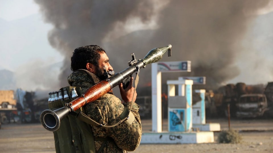 Soldat mit Panzerfaust vor brennendem Gebäude.