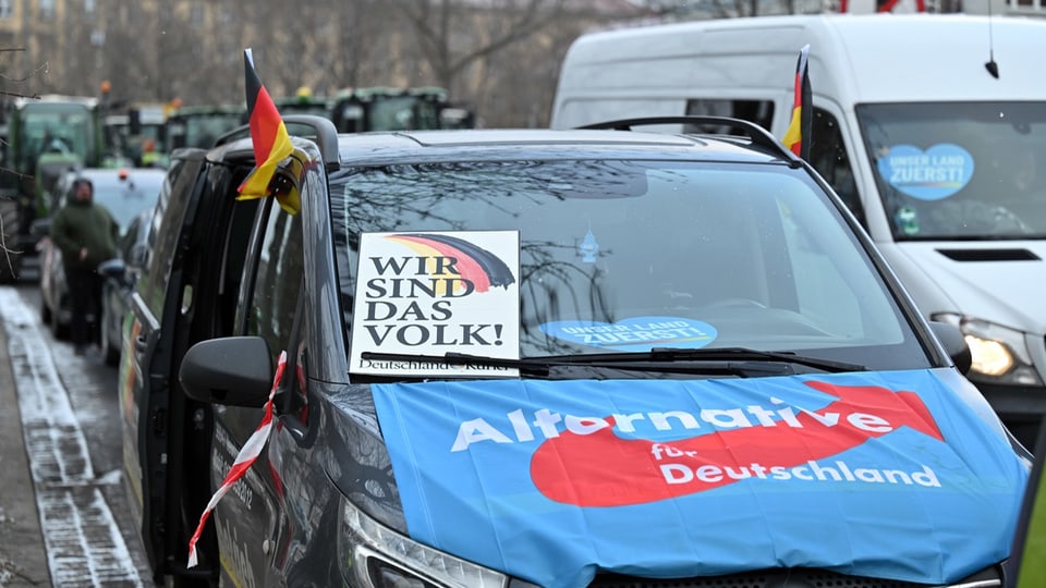 Ein Auto mit einem Plakat, auf dem steht: Wir sind das Volk, und auf dessen Kühlerhaube eine Afd-Fahne liegt.