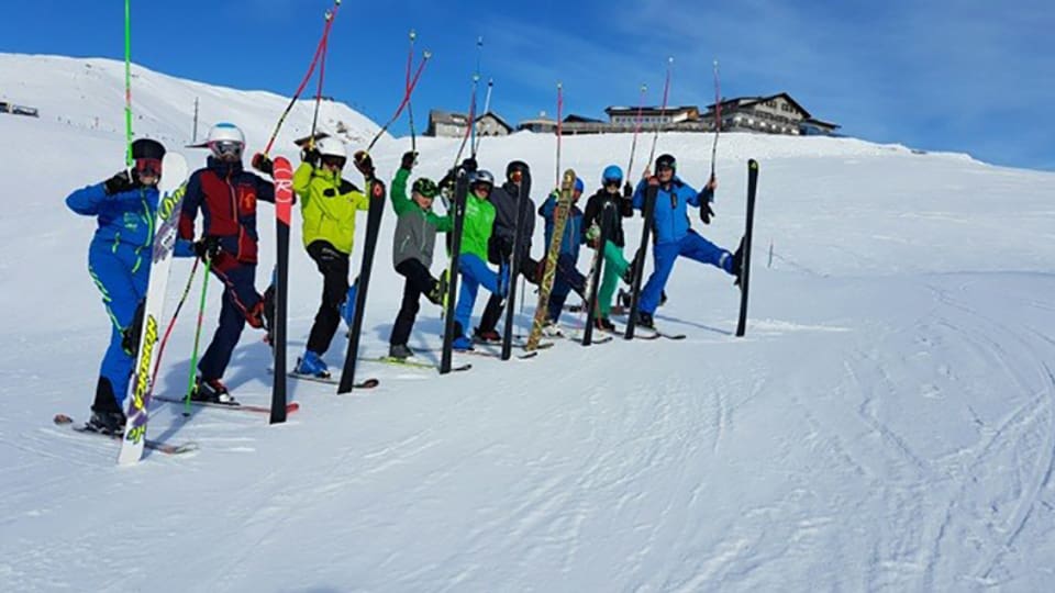 Eine Gruppe von Kindern stehen auf der Skipiste und strecken ihre Skistöcke in die Luft