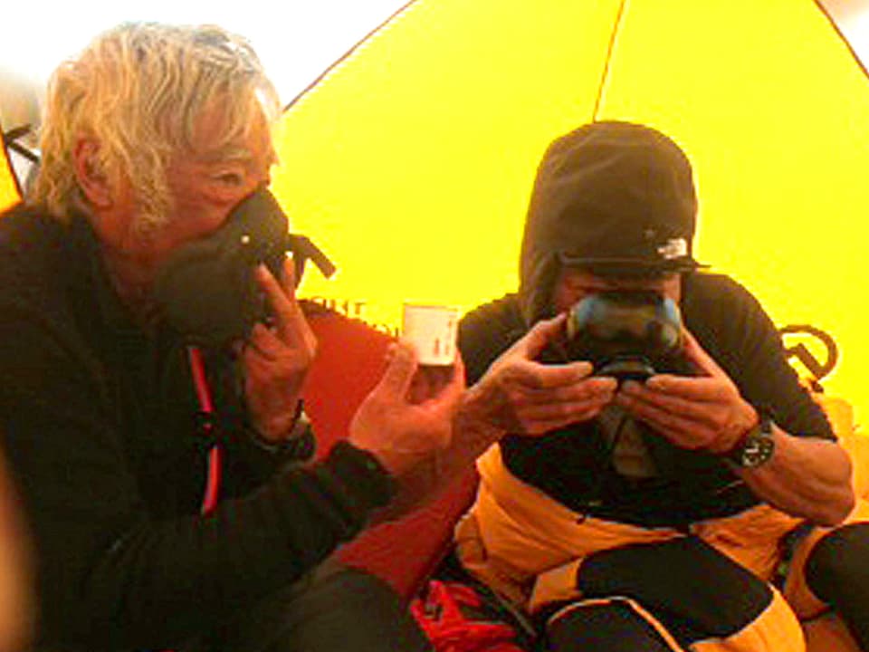 Der 80jährige Japaner Yuichiro Miura hält sich eine Sauerstoffmaske vor das Gesicht. Ebenso sein Sherpa.