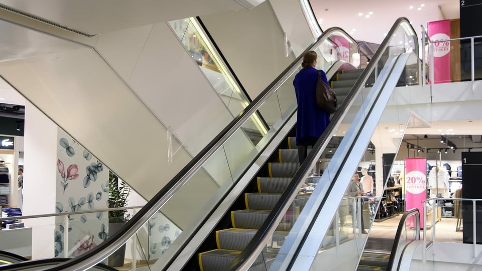Eine einzelne Person auf einer Rolltreppe in einem Geschäft.
