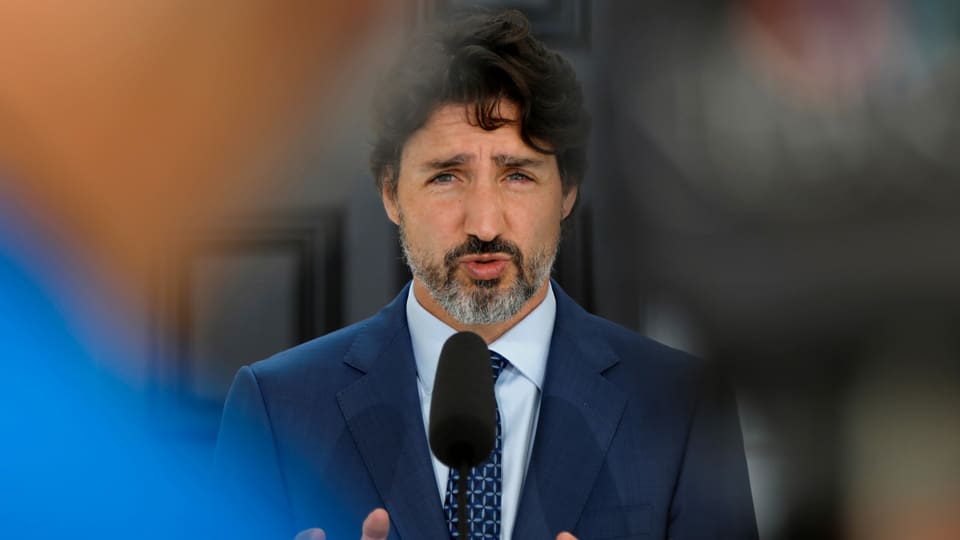 Trudeau (mit Bart) spricht in ein Mikrofon.