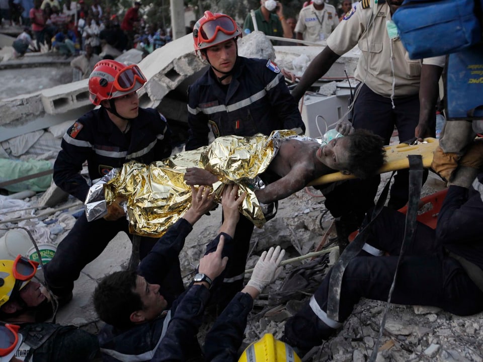 Rettungskräfte tragen eine Verletzte auf einer Liege aus den Trümmern.