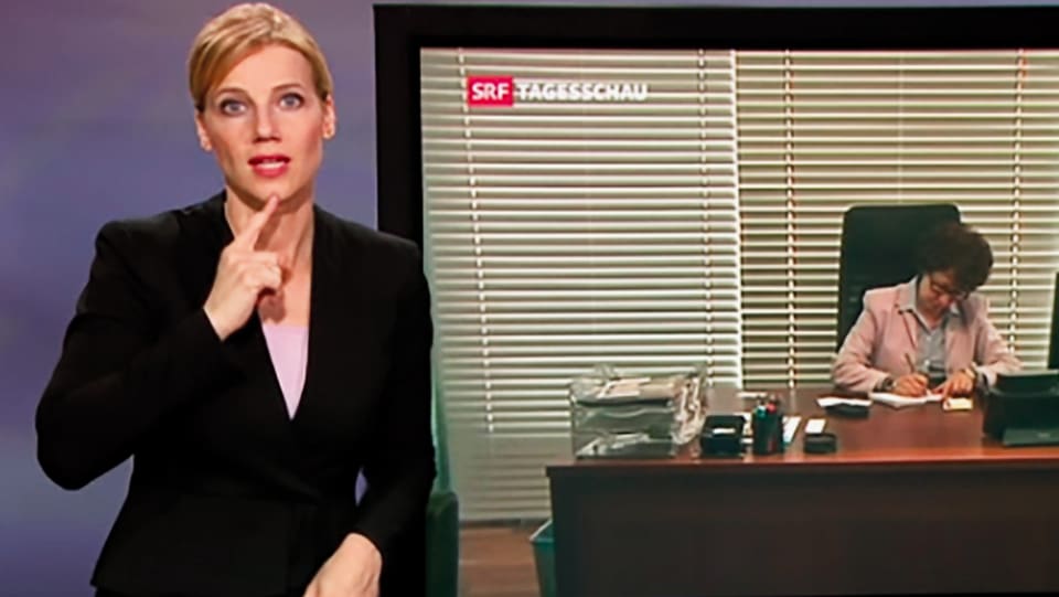 Gebärdendolmetscherin neben TV-Bildschirm stehend und artikulierend.