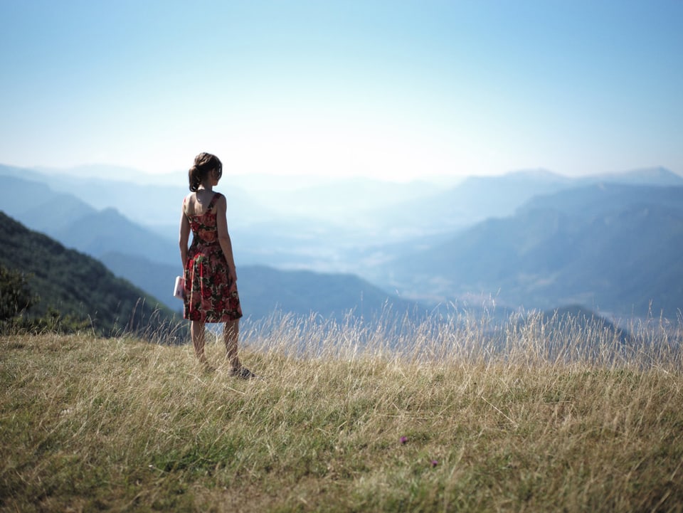 Eine Frau steht auf einer Wiese und blickt auf eine wunderschöne Landschaft hinab.
