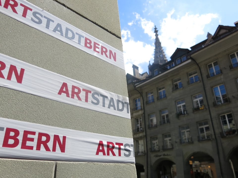 Hinweis auf ArtStadtBern an einer Mauer; dahinter Altstadt und Münster