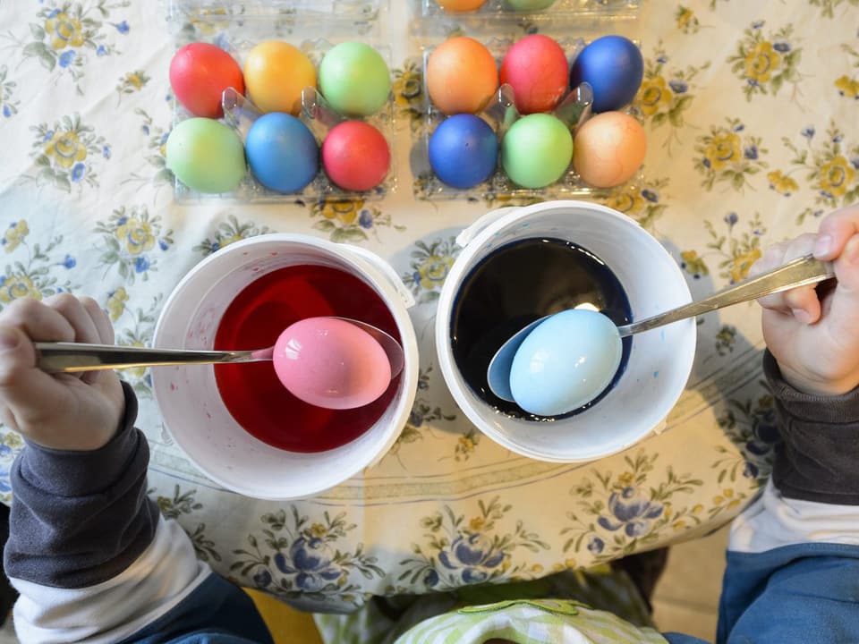 Eier werden in zwei Gefässen mit unterschiedlichen Farben gefärbt.