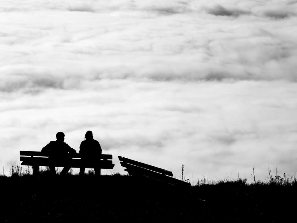 Zwei Menschen sitzen oberhalb des Nebelmeers auf einer Bank.