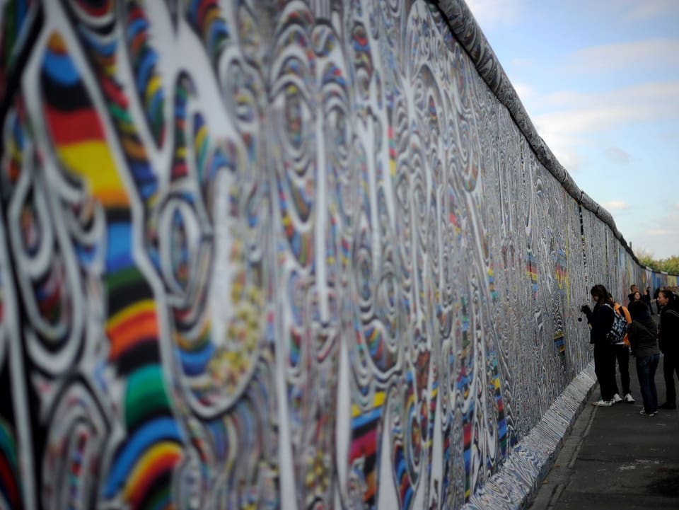 Passanten vor der bemalten Berliner Mauer.