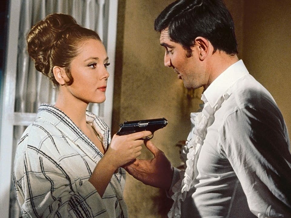 Bond-Girl bedroht 007 mit Schusswaffe. 