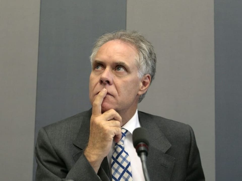 Mann mit grauen Haaren im grauen Anzug vor einer grauen Wand.