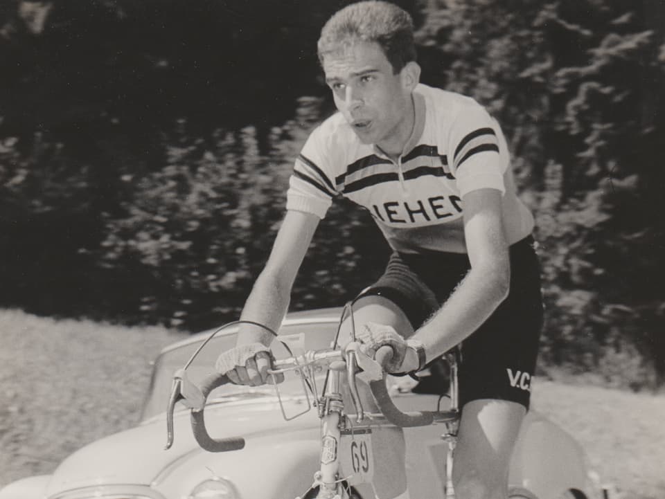 Kurt Kaiser im Jahr 1964 auf dem Fahrrad, im Hintergrund sieht man ein altes Auto.