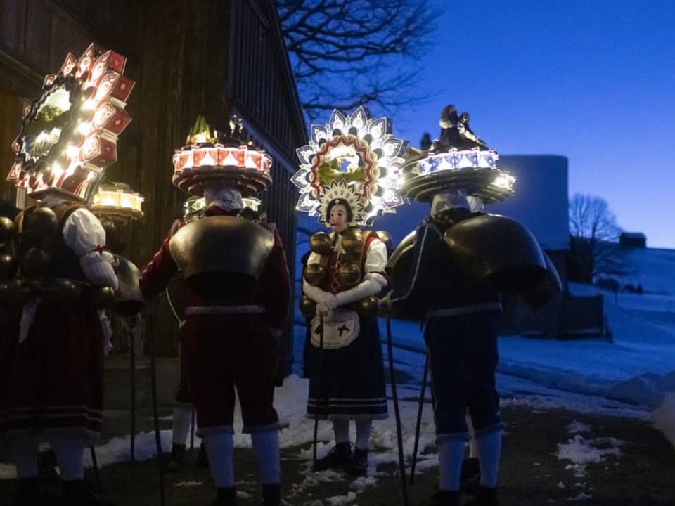 Eine Gruppe Kostümierter mit beleuchteten Hauben in der Morgendämmerung.