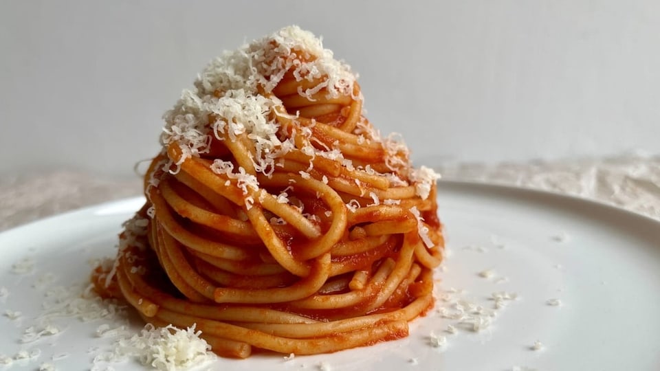 Spaghettti mit Tomatensauce mittig auf einem Teller angerichtet.