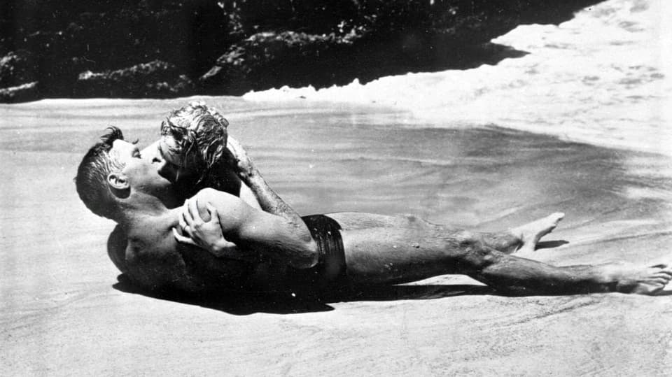 Zwei junge Menschen küssen sich liegend am Strand.