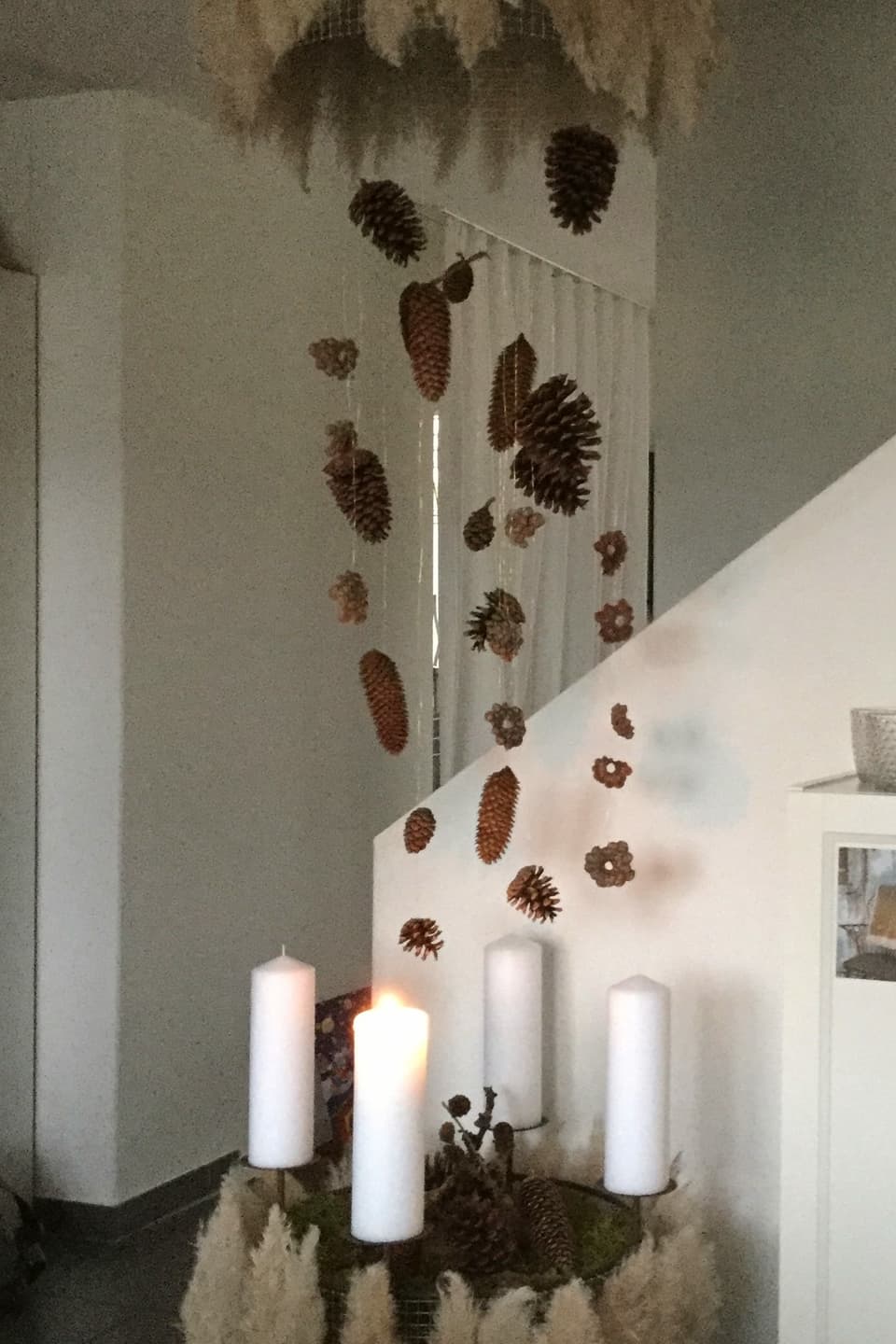 Tannenzapfen hängen in der Luft über vier weissen Kerzen.