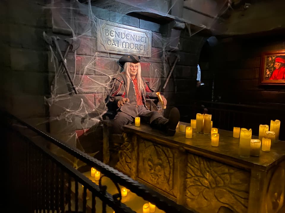 Ein langhaariger Pirat ist von Spinnweben umgeben und sitzt auf einem Altar, auf dem viele Kerzen stehen.