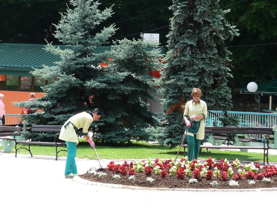 Zwei Frauen graben ein grosses Blumenbeet auf der Strasse um. 