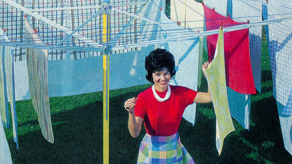 Eine Frau im Look der 50er hängt Wäsche auf.