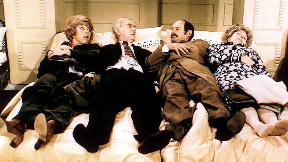 Vier Personen liegen auf einem Bett und schauen sich gegenseitig an