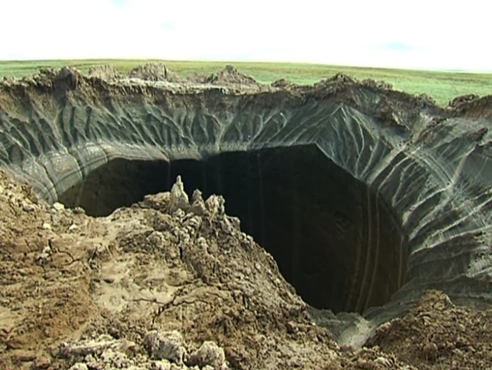 Ein grosses Loch klafft in der Erde. Die Seitenwände sehen schwarz und bedrohlich aus. Wasser tropft in den Krater, ein Zeichen des schmelzenden Permafrosts.