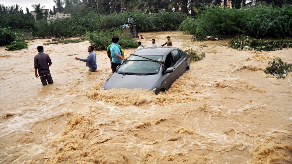 Ein Auto und mehrere Menschen stehen im Hochwasser in Karachi.
