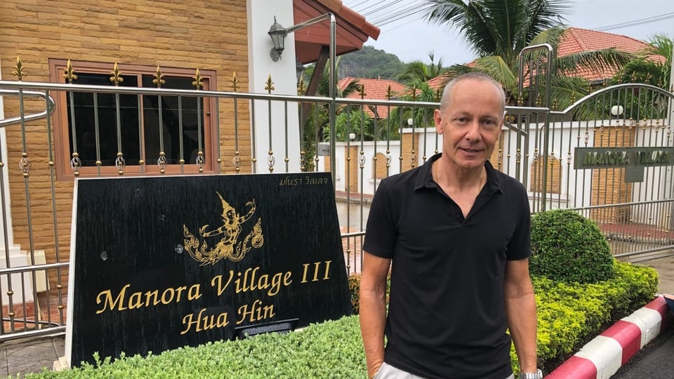 Walter Camenisch vor einer Tafel vor dem Resort Manora Village