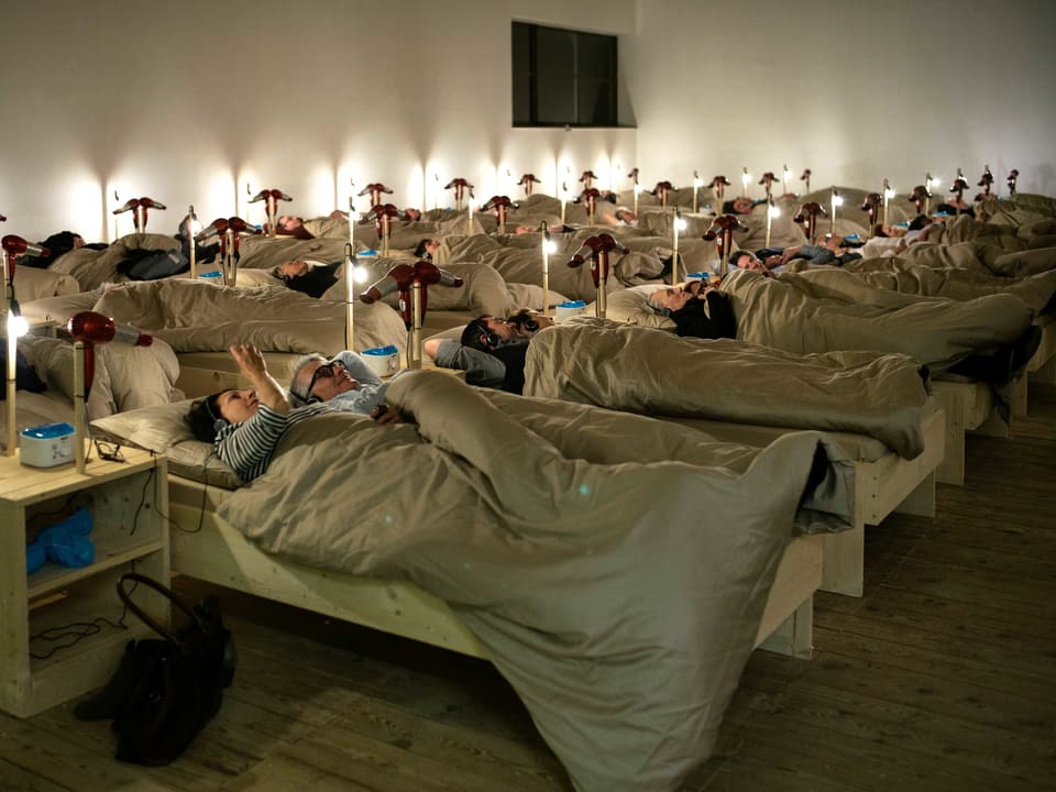 Leute liegen in Betten im Museumsaal.