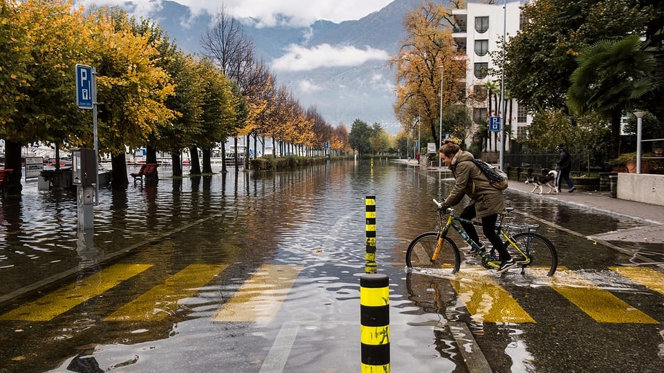Faru mit Velo fäht auf überschwemmter Strasse in Locarno.