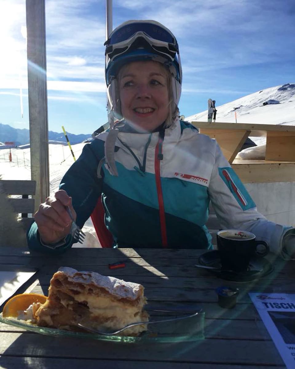 Eine Frau in Skikleidern sitzt vor einer grossen Crèmeschnitte.