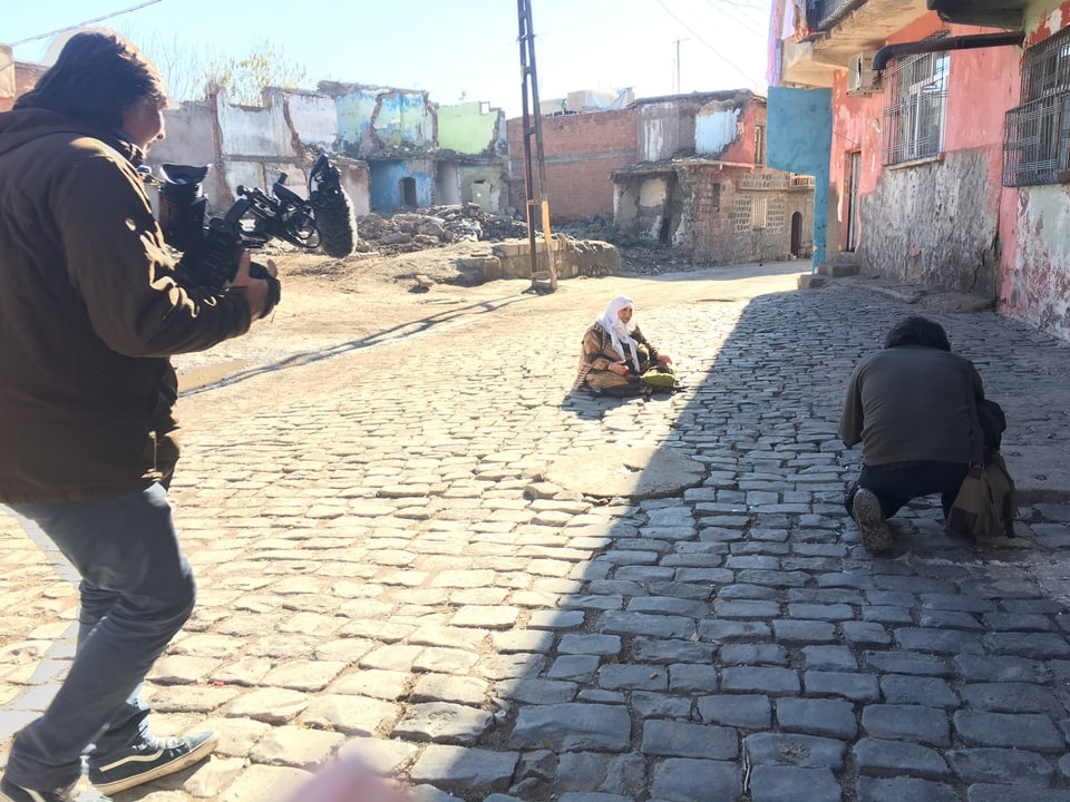 Eine kurdische Frau sitzt auf dem Boden, während sie von einem Filmteam gefilmt wird.