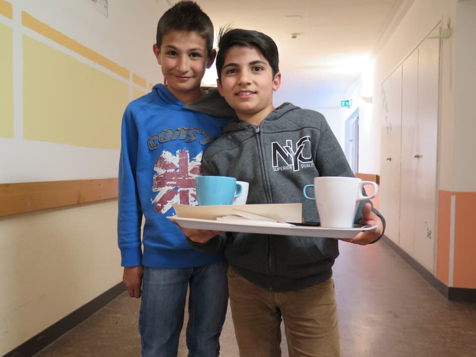 Zwei Jungen halten ein Tablett mit Kaffeetassen
