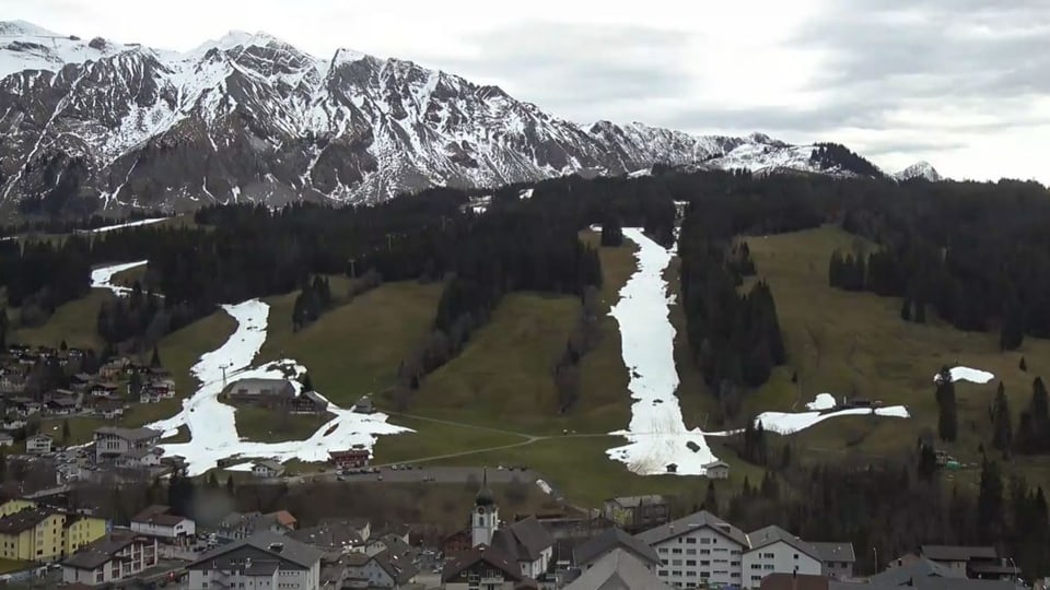 Grüner Hang über dem Dorf Sörenberg mit zwei weissen Schneebändern