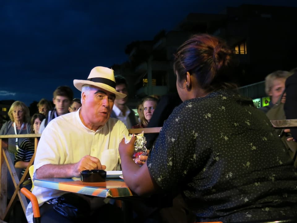 Eine Frau und ein Mann essen in einem Restaurant, daneben passieren die Besucher.