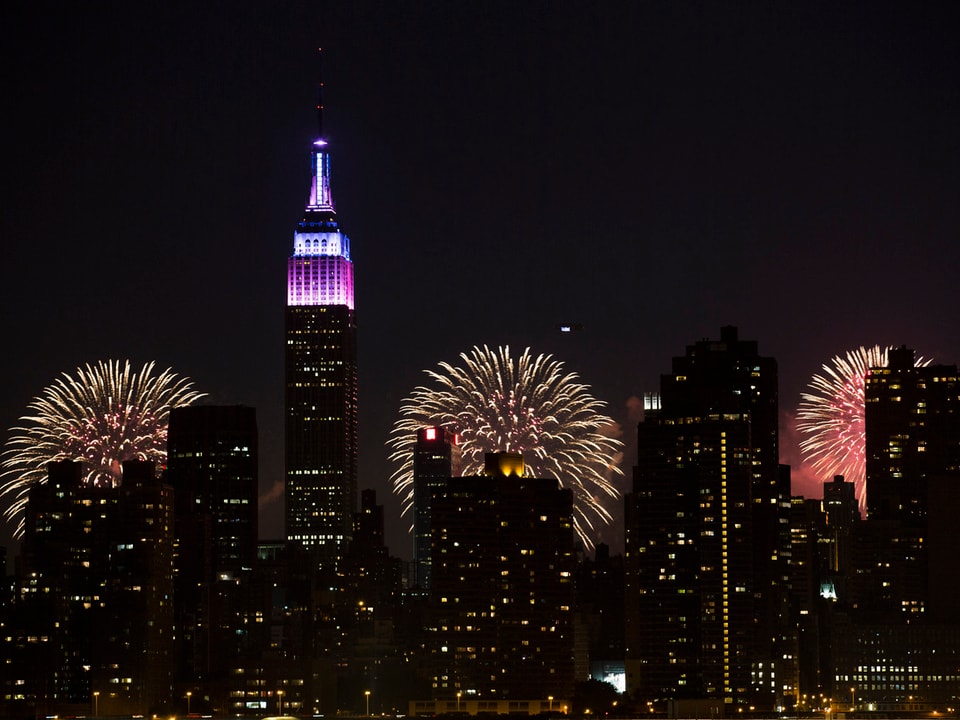 Feuerwerk erleuchtet den Nachthimmel von New York, davor steht das beleuchtete Empire State Building.