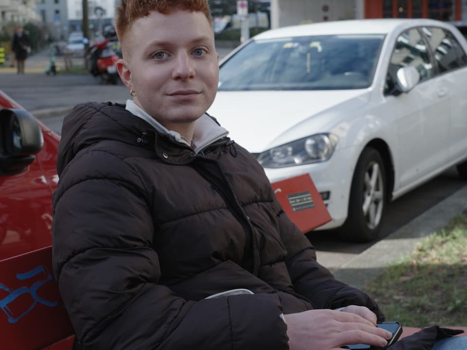 Nicolas, ein junger Mann, sitzt auf einer Parkbank und lächelt milde in die Kamera.