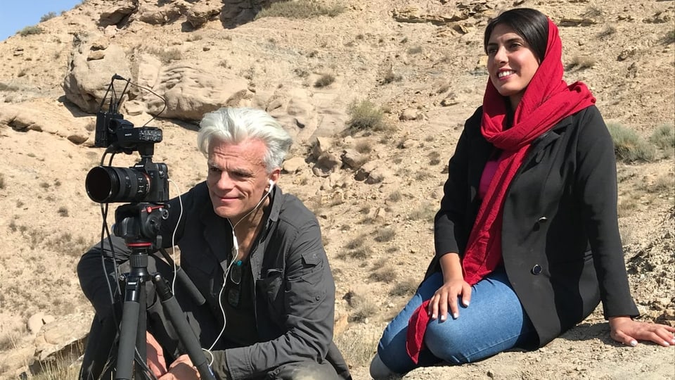 Ein Mann und eine Frau sitzen auf Geröll und filmen in der Wüste.