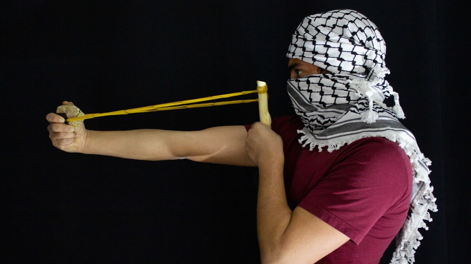 Mann mit Palästinensertuch und gespannter Steinschleuder