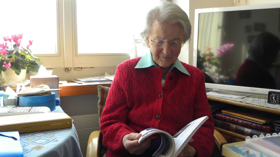 Die Seniorin sitzt am Tisch in ihrem Zimmer und blättert in einer Zeitschrift.
