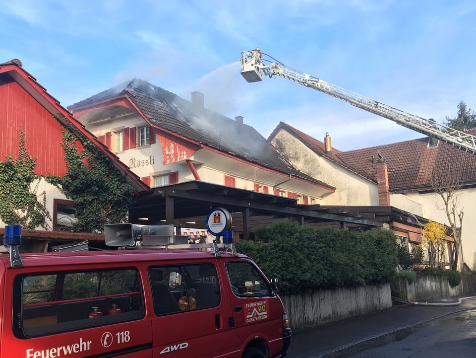 Feuerwehrmann steht auf Drehleiter und spritzt Wasser von oben auf das Dach