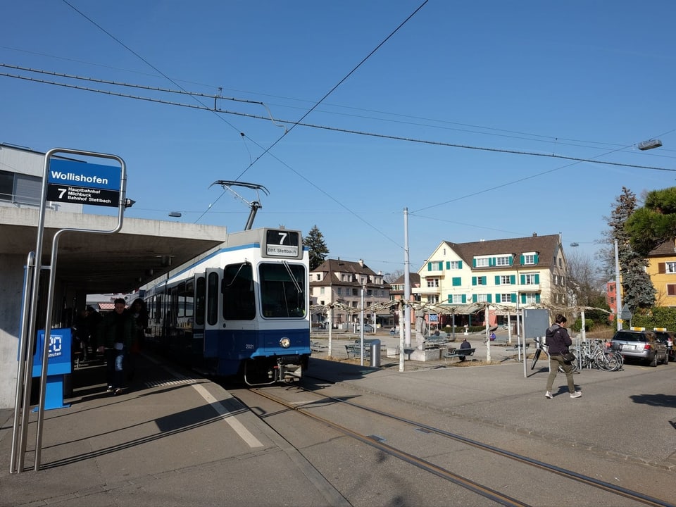Ein blau-weisses Tram steht an der Haltestelle, daneben ein grosser Platz, der von Häusern umgeben ist.