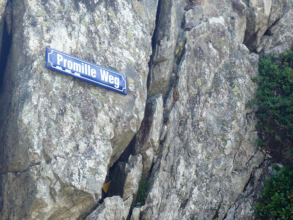 Auf einem Schild an einer Felswand steht Promille Weg.